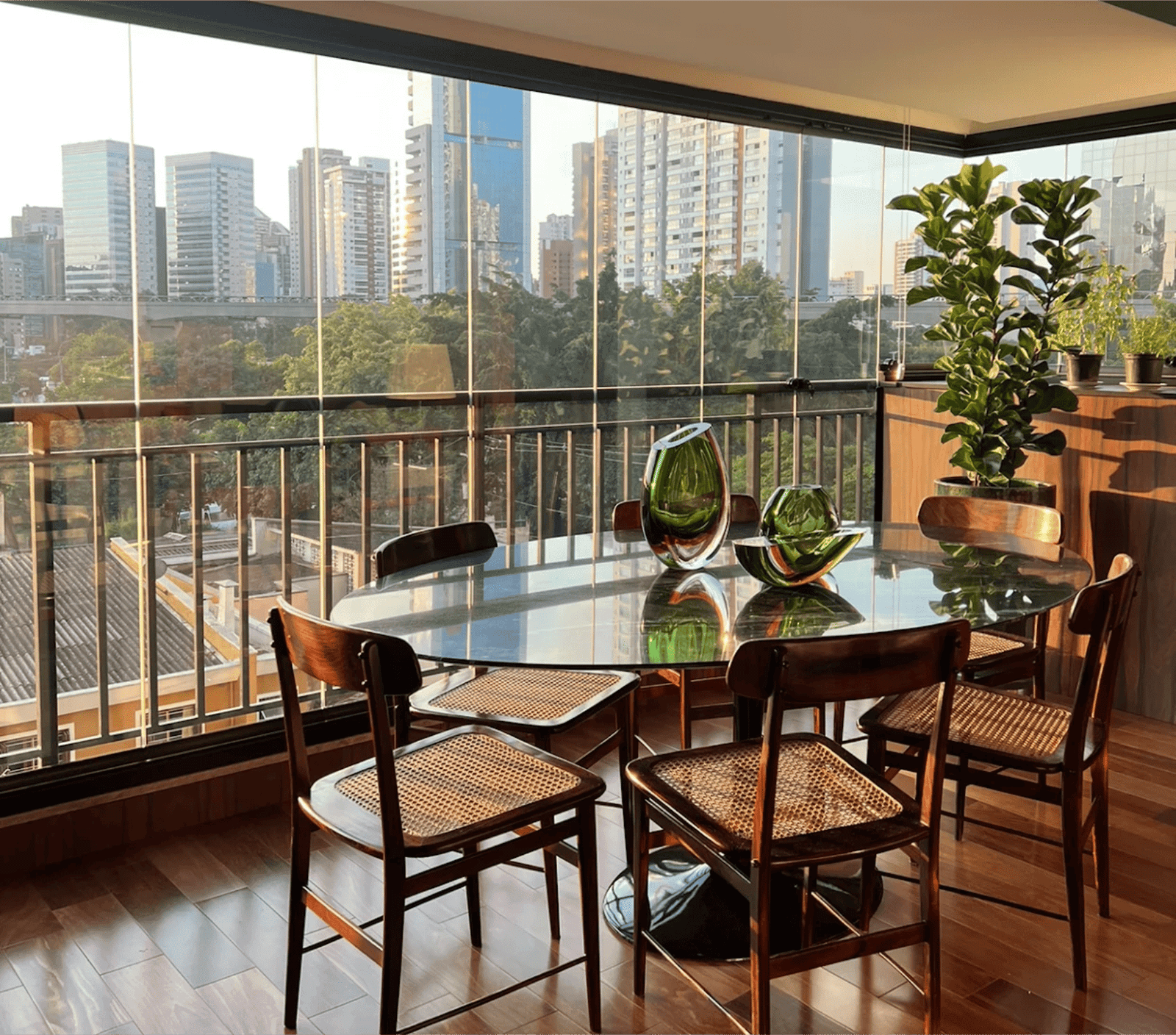 Varanda envidraçada com mesa de jantar e vista da cidade ao entardecer